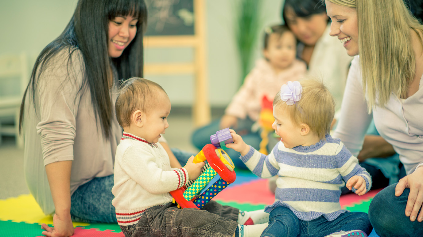 Im Mütter-Treff: Drei Mütter beobachten entspannt lachend ihre Kleinkinder beim Spiel.