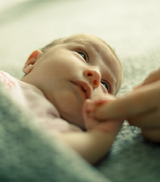 Ein Säugling im Bettchen umfasst den Finger der Mutter und sieht sie intensiv an.